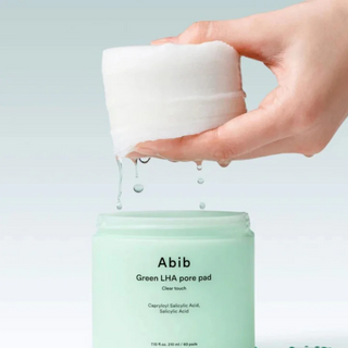 a hand squishing Abib Green LHA Pore Pads above the open container